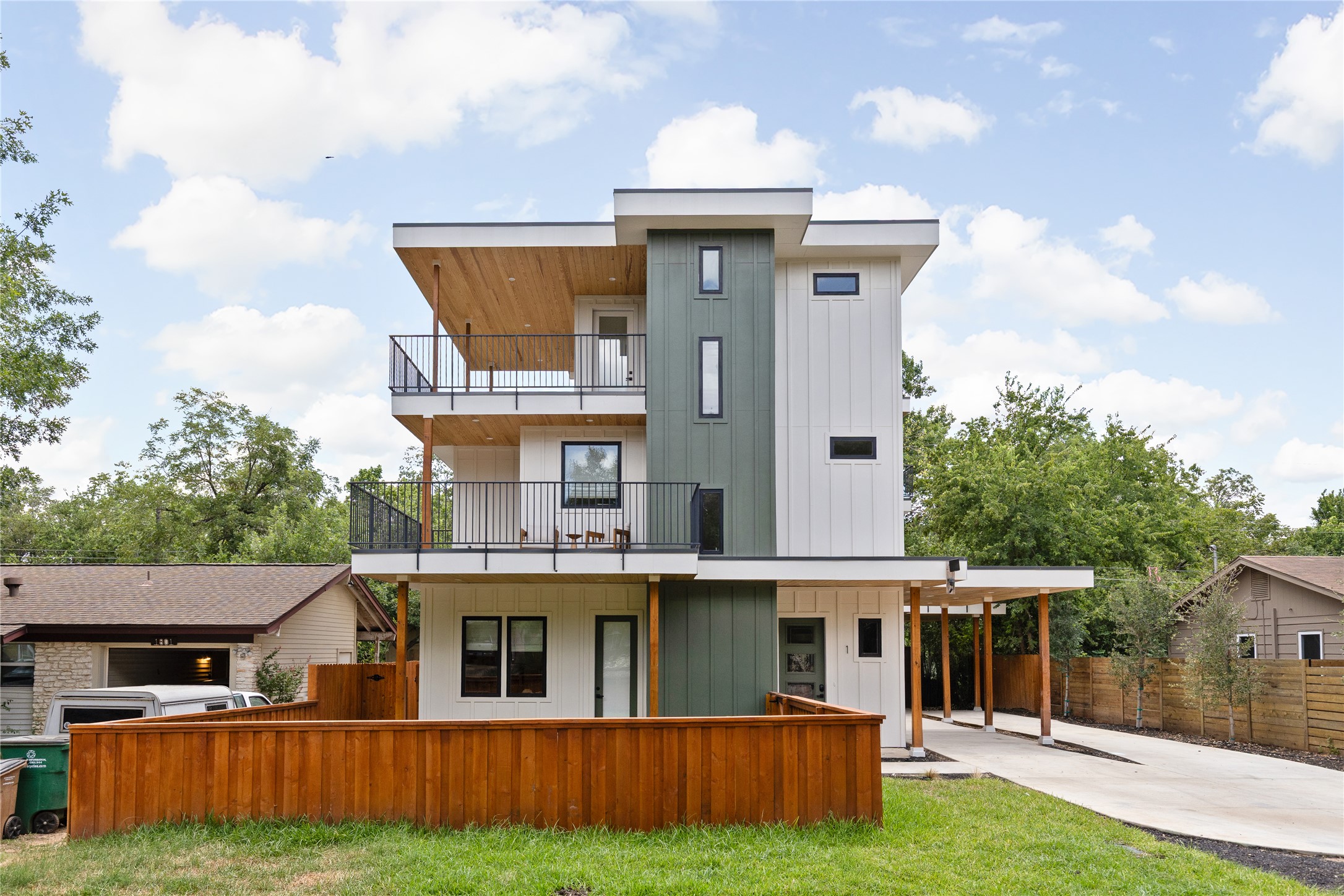 Rear view of house with board and batten siding, a balcony, a patio, driveway, and an attached carport