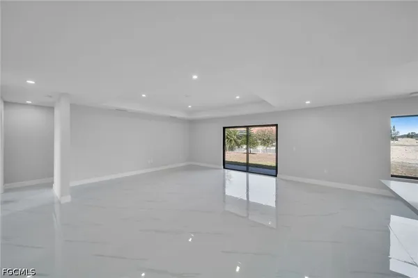 an empty room with windows and view of kitchen