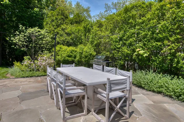a patio with table and chairs with potted plants and large trees