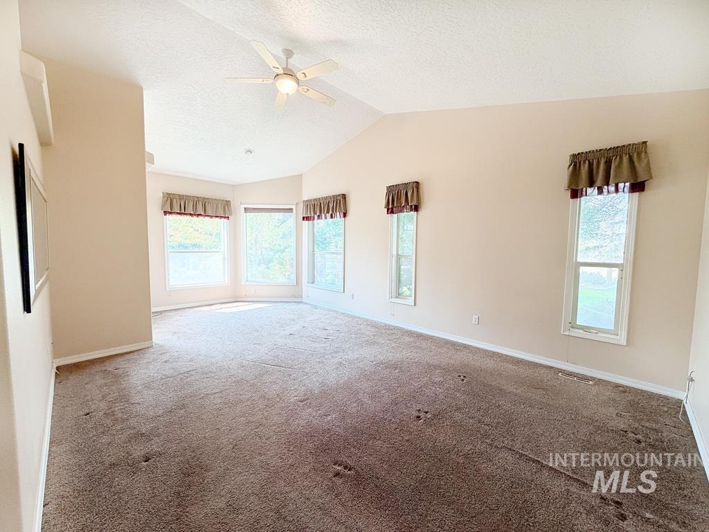 5875 Diamond Ridge Way Nampa, ID 83686 - Photo 20 of 32 Spacious great room with vaulted ceiling and ceiling fan, abundant natural light from multiple windows and glass doors, and neutral carpet flooring throughout