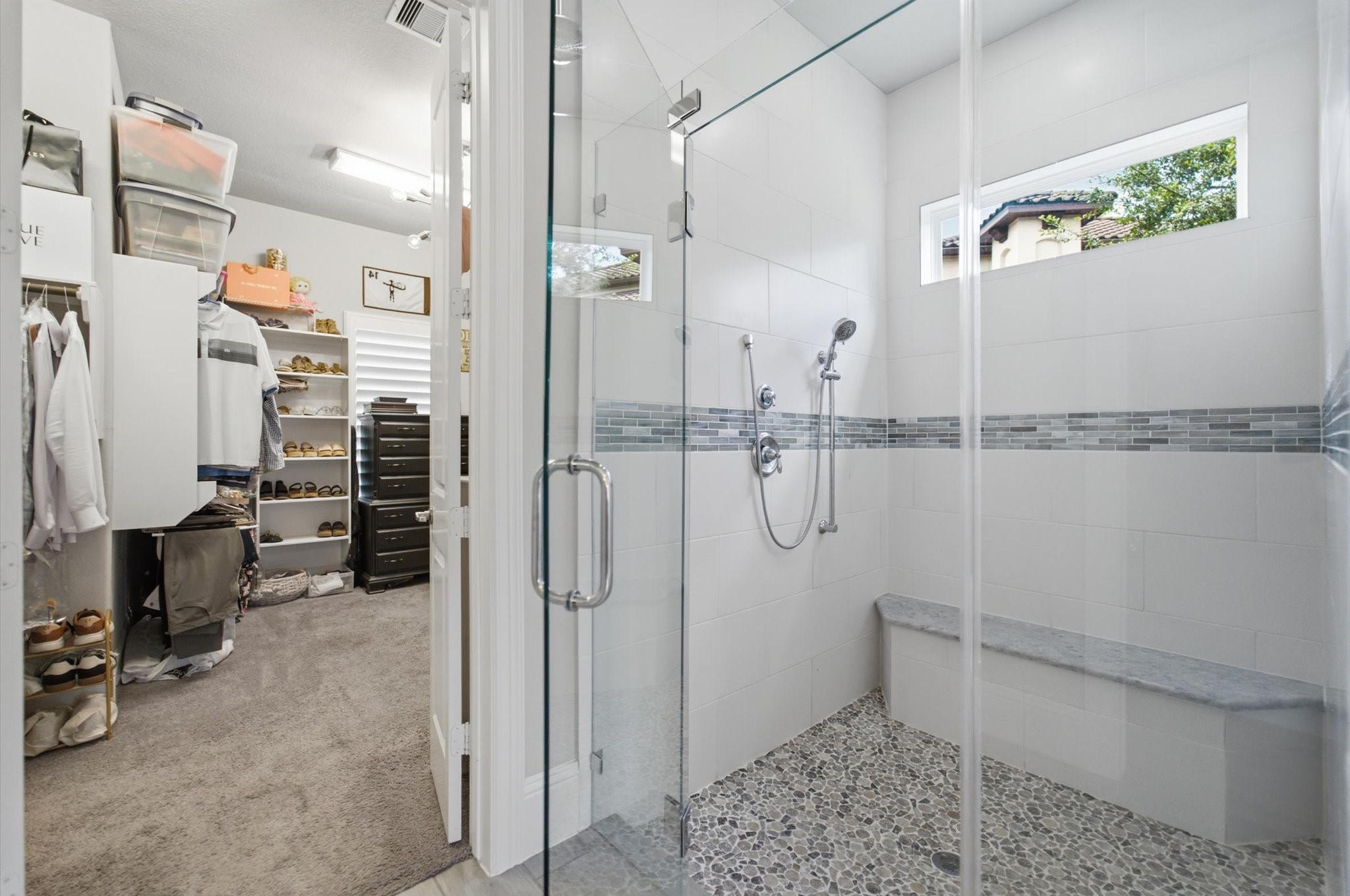 23722 Thortons Park Lane Spring, TX 77389 - Photo 15 of 48 This photo showcases a modern walk-in shower with a glass door, decorative tile accents, and a built-in bench. Adjacent is a spacious walk-in closet with shelving and ample storage space, making it ideal for organization and convenience.
