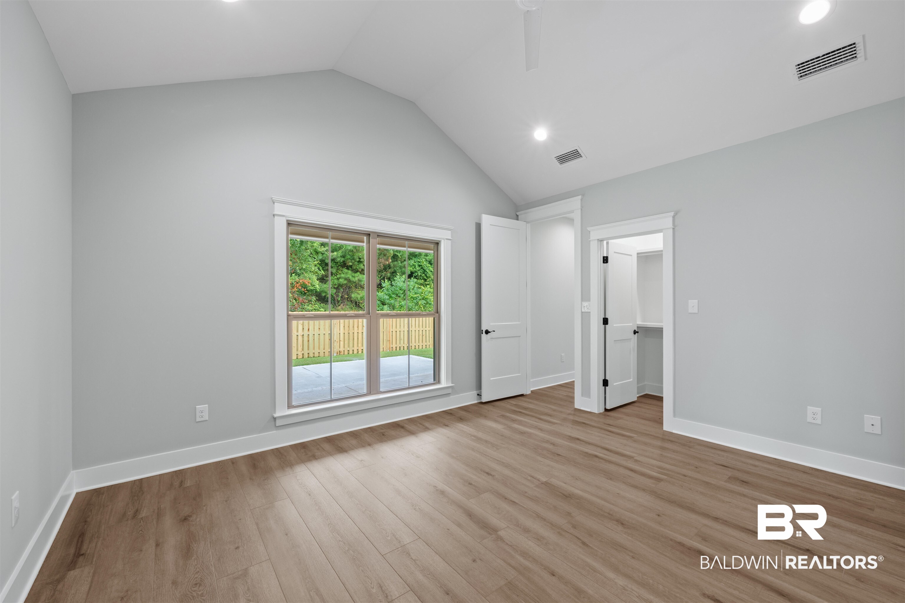 27494 Patch Pl Loop Daphne, AL 36526 - Photo 13 of 26 Vaulted ceiling room featuring wood-finish flooring, recessed lighting, and a window overlooking a fenced patio