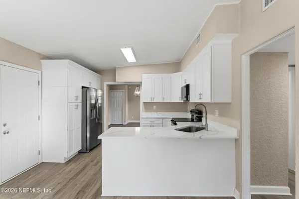 a kitchen with stainless steel appliances kitchen island granite countertop a sink dishwasher stove and white cabinets with wooden floor