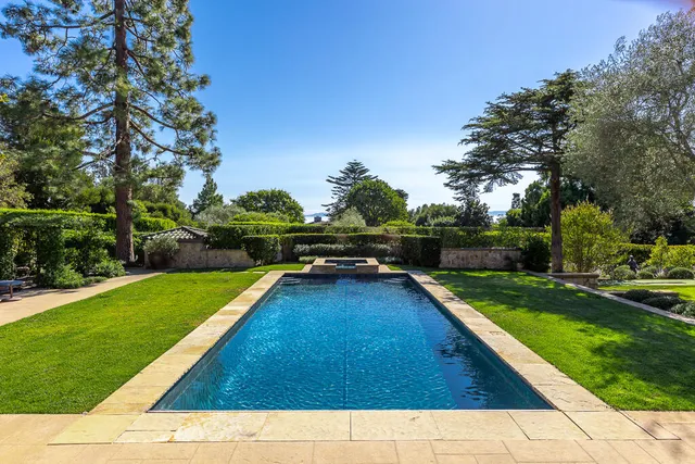 a view of a swimming pool with lawn chairs and a large tree