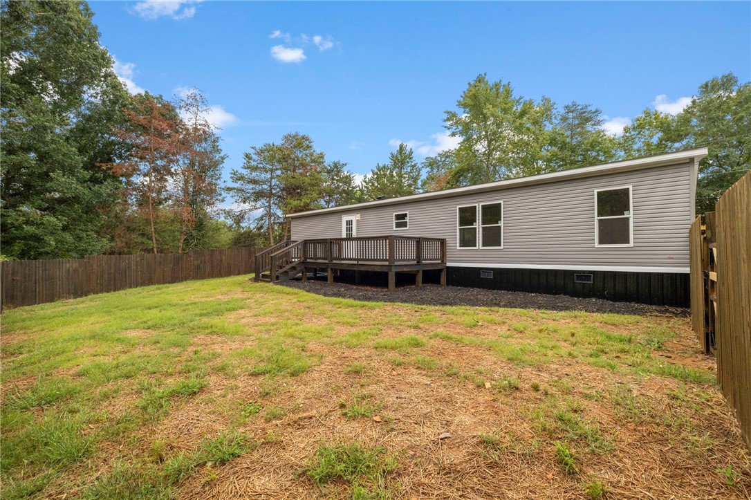 474 Bryant Road Pelzer, SC 29669 - Photo 41 of 44 An expansive backyard features a wooden deck and a complete privacy fence under blue skies.