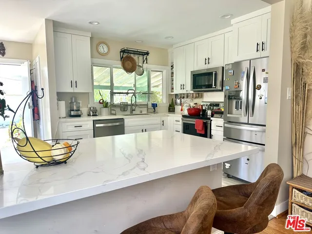 a living room with stainless steel appliances furniture a large window and a kitchen view
