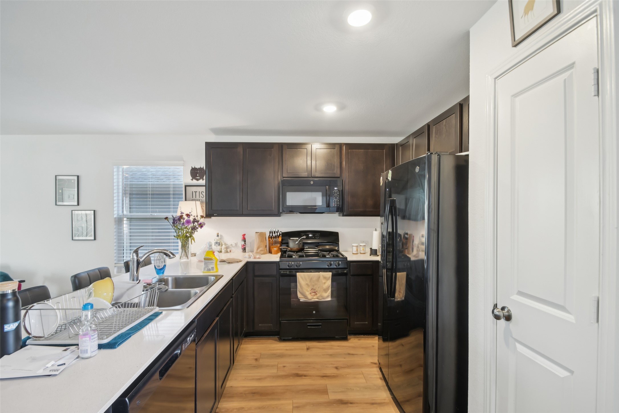 857 Powell Kyle, TX 78640 - Photo 10 of 28 Kitchen with black appliances, light countertops, light wood-style floors, dark wood finish cabinets, and a kitchen bar