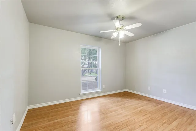 an empty room with wooden floor fan and window