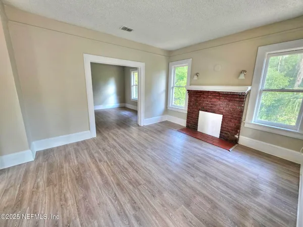 an empty room with wooden floor fireplace and windows