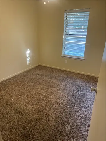 an empty room with wooden floor kitchen view and windows