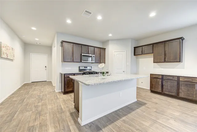 a kitchen with stainless steel appliances granite countertop a stove top oven a sink dishwasher and a refrigerator with wooden floor