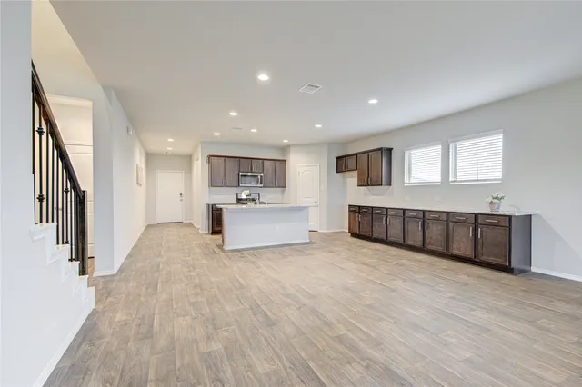 a view of an empty room with wooden floor and a kitchen