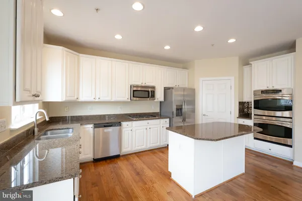 a large kitchen with granite countertop a stove a sink a refrigerator and white cabinets with wooden floor
