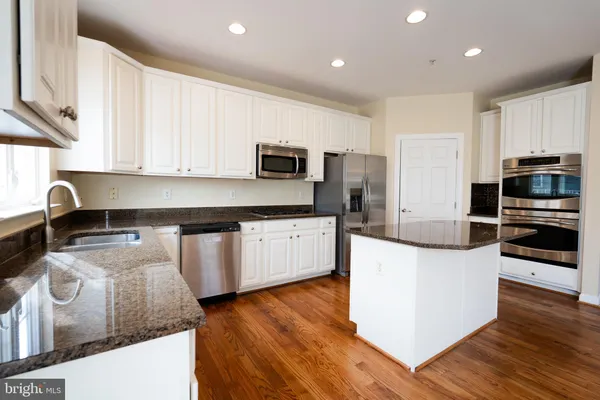 a kitchen with stainless steel appliances granite countertop a stove top oven a sink a refrigerator white cabinets and wooden floor