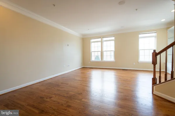 an empty room with wooden floor and windows with curtains