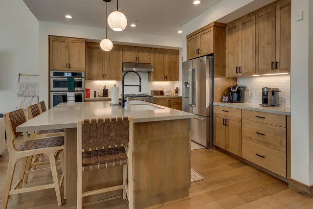 a large kitchen with stainless steel appliances a stove a sink dishwasher a living room with couches chairs and a large window with wooden floor