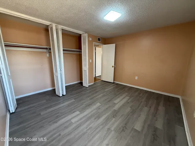a view of an empty room with wooden floor and a refrigerator