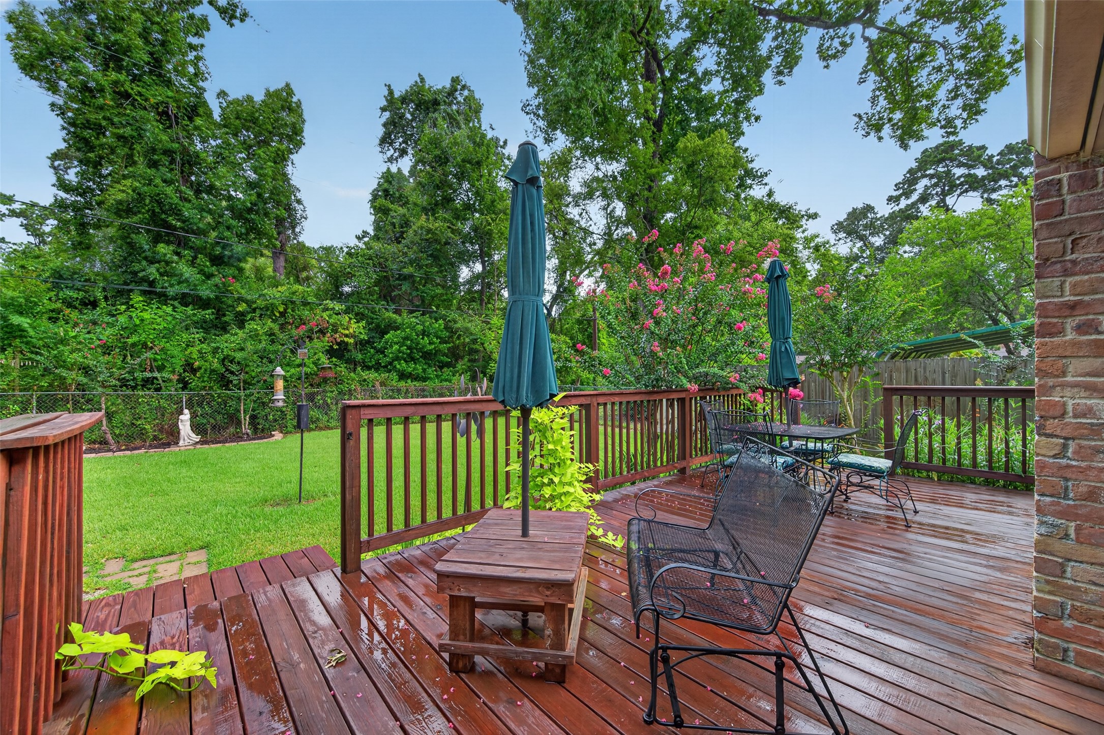 24719 Wilderness Road Spring, TX 77380 - Photo 38 of 42 This photo showcases a beautiful backyard deck with wooden flooring, surrounded by lush greenery and flowering plants. It features a perfect space for relaxation and entertaining.