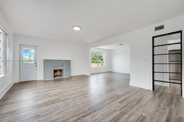 an empty room with wooden floor fireplace and windows