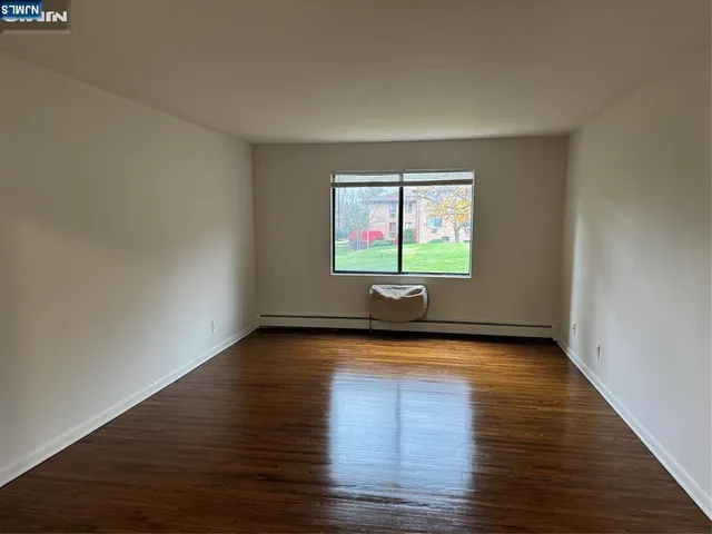 a view of an empty room with wooden floor and windows