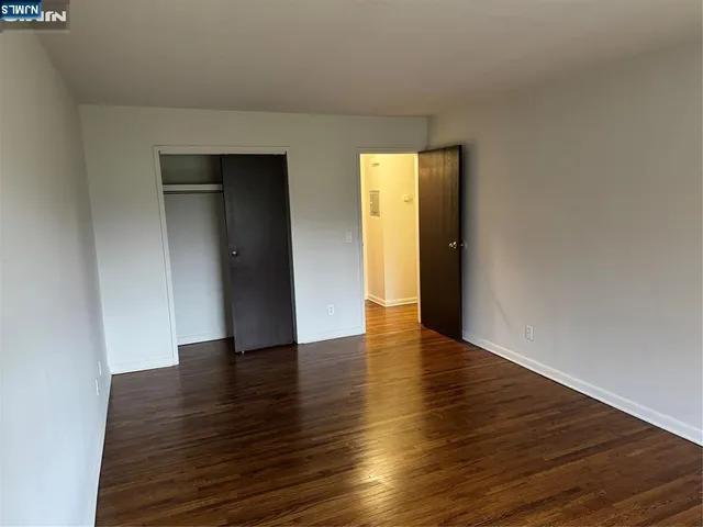 a view of an empty room with wooden floor and closet