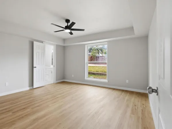 an empty room with wooden floor ceiling fan and windows