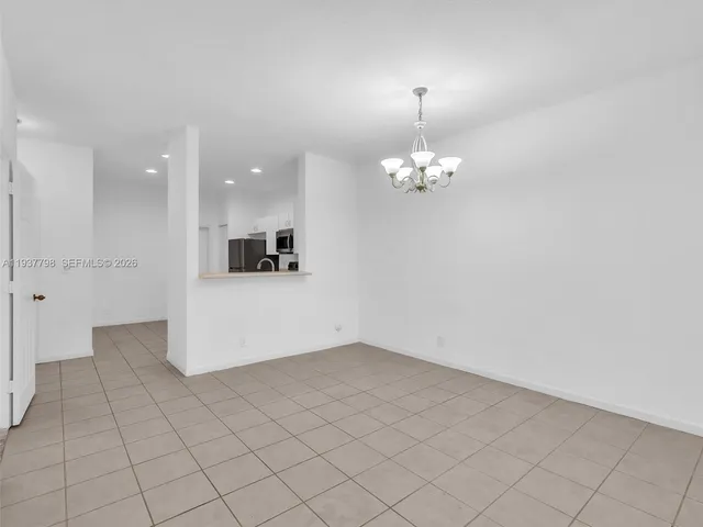 an empty room with kitchen view and a chandelier