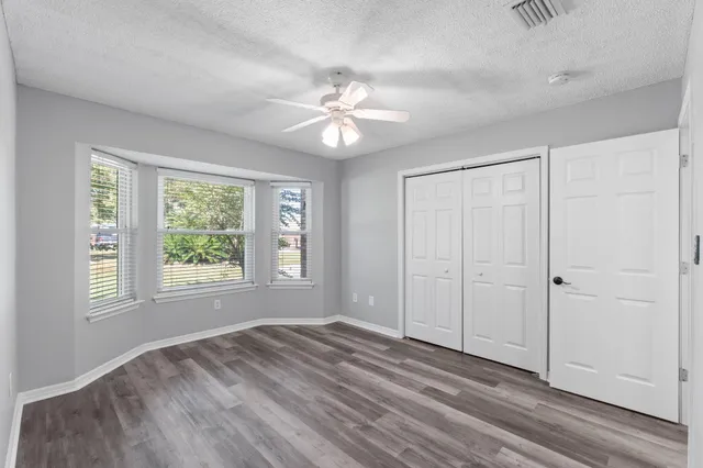 an empty room with wooden floor ceiling fan and windows