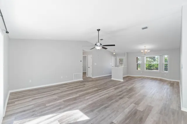 an empty room with wooden floor ceiling fan and windows