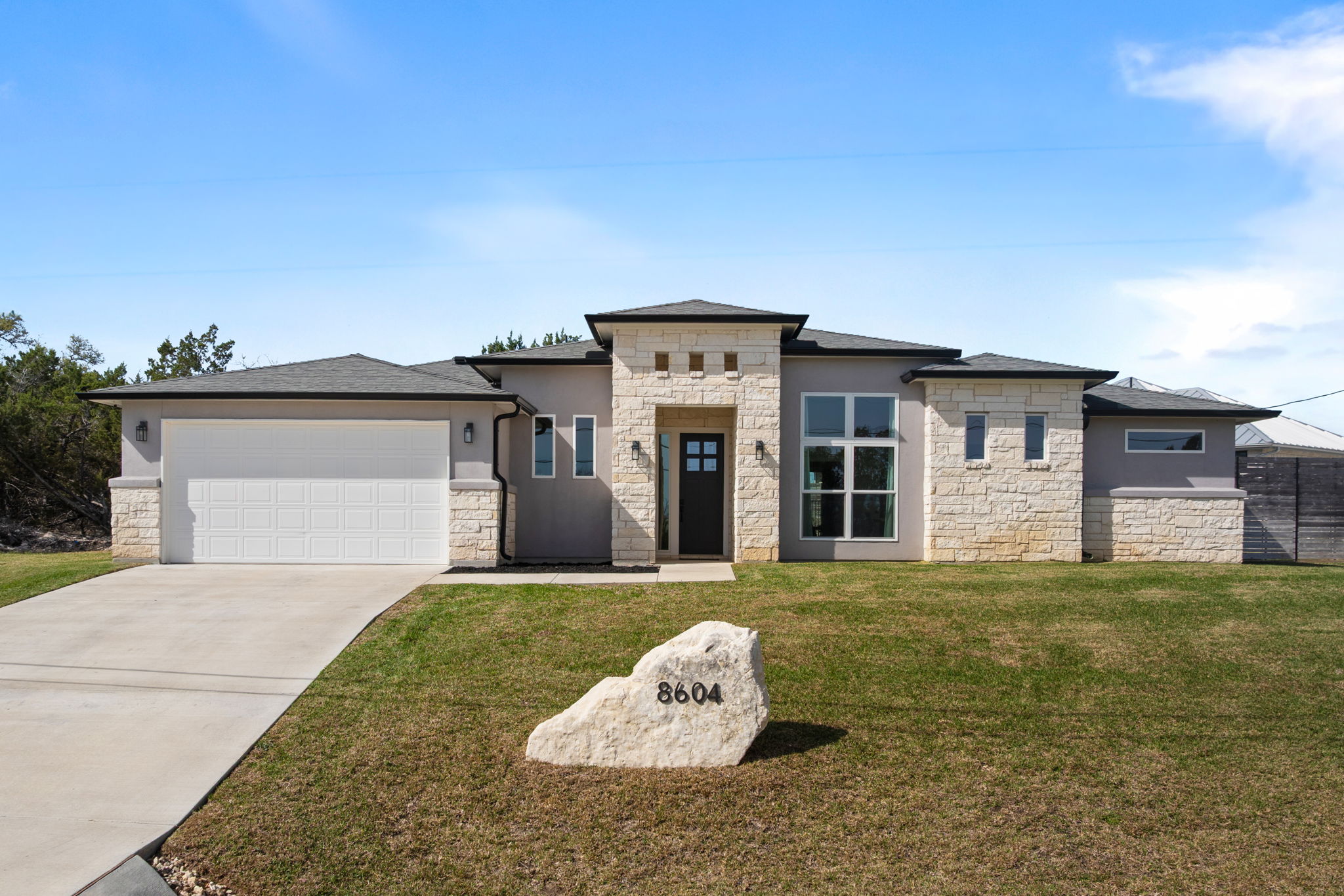 Prairie-style house featuring stone siding, concrete driveway, a front yard, stucco siding, and an attached garage