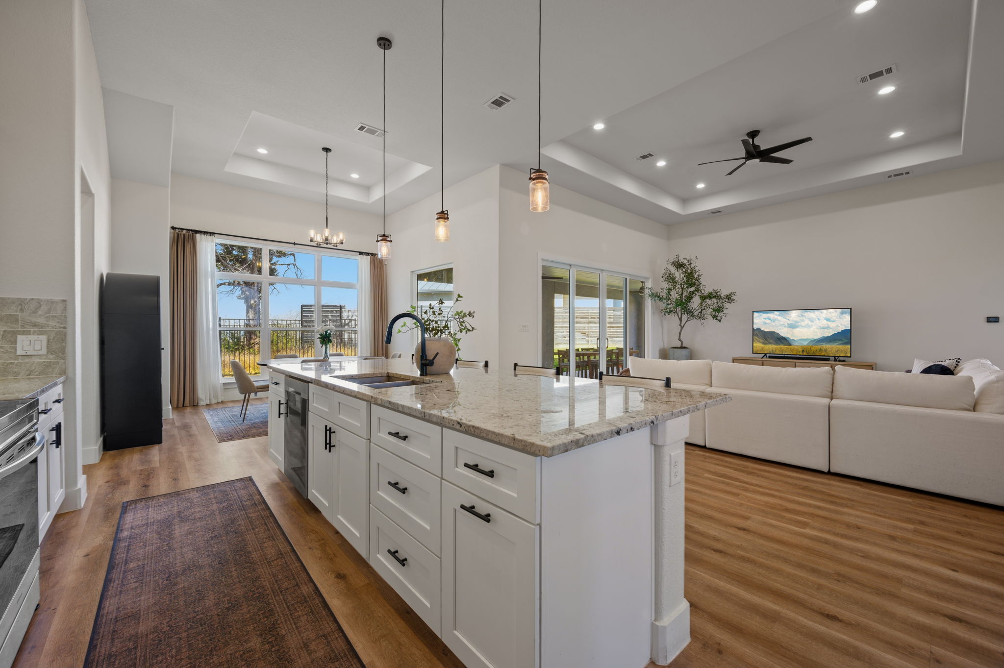 8604 Bar K Ranch Road Lago Vista, TX 78645 - Photo 9 of 37 Kitchen with white cabinets, light stone countertops, an island with sink, light wood-type flooring, and a raised ceiling