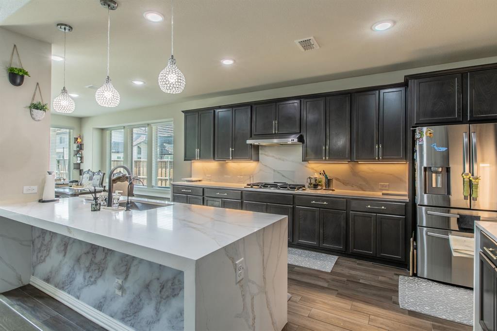 2521 Maidenhair Road Frisco, TX 75033 - Photo 5 of 39 Kitchen featuring a large waterfall island with a stone countertop, dark cabinetry, stainless steel appliances, and wood-finish flooring