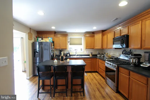 a kitchen with stainless steel appliances granite countertop a refrigerator a sink dishwasher a stove a dining table and chairs with wooden floor