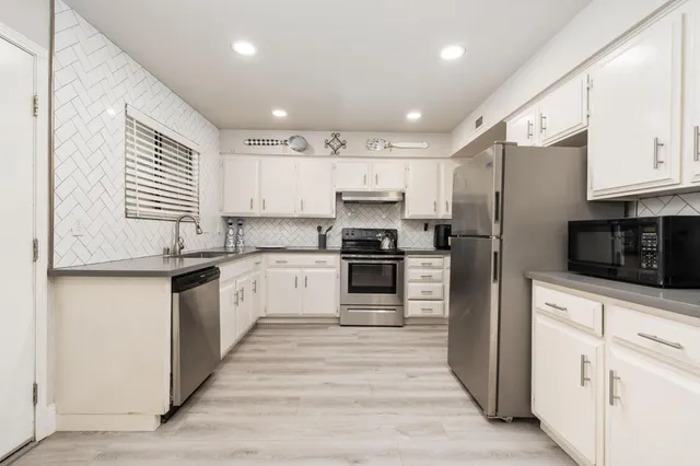 a kitchen with granite countertop a refrigerator oven a sink dishwasher and white cabinets with wooden floor