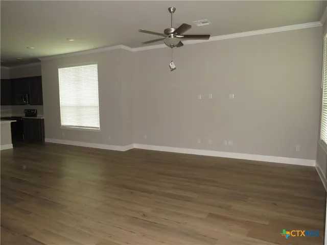 an empty room with wooden floor fan and windows