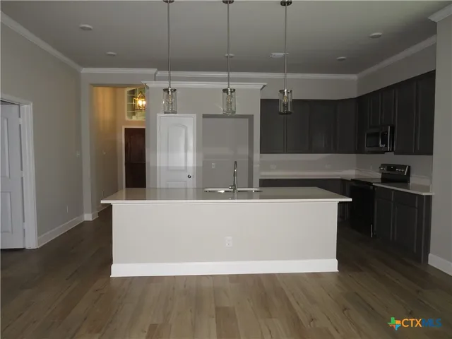 a living room with stainless steel appliances kitchen island granite countertop a refrigerator a stove and a wooden floors