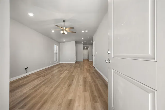 a view of an empty room with wooden floor and fan