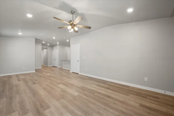 an empty room with wooden floor chandelier fan and windows