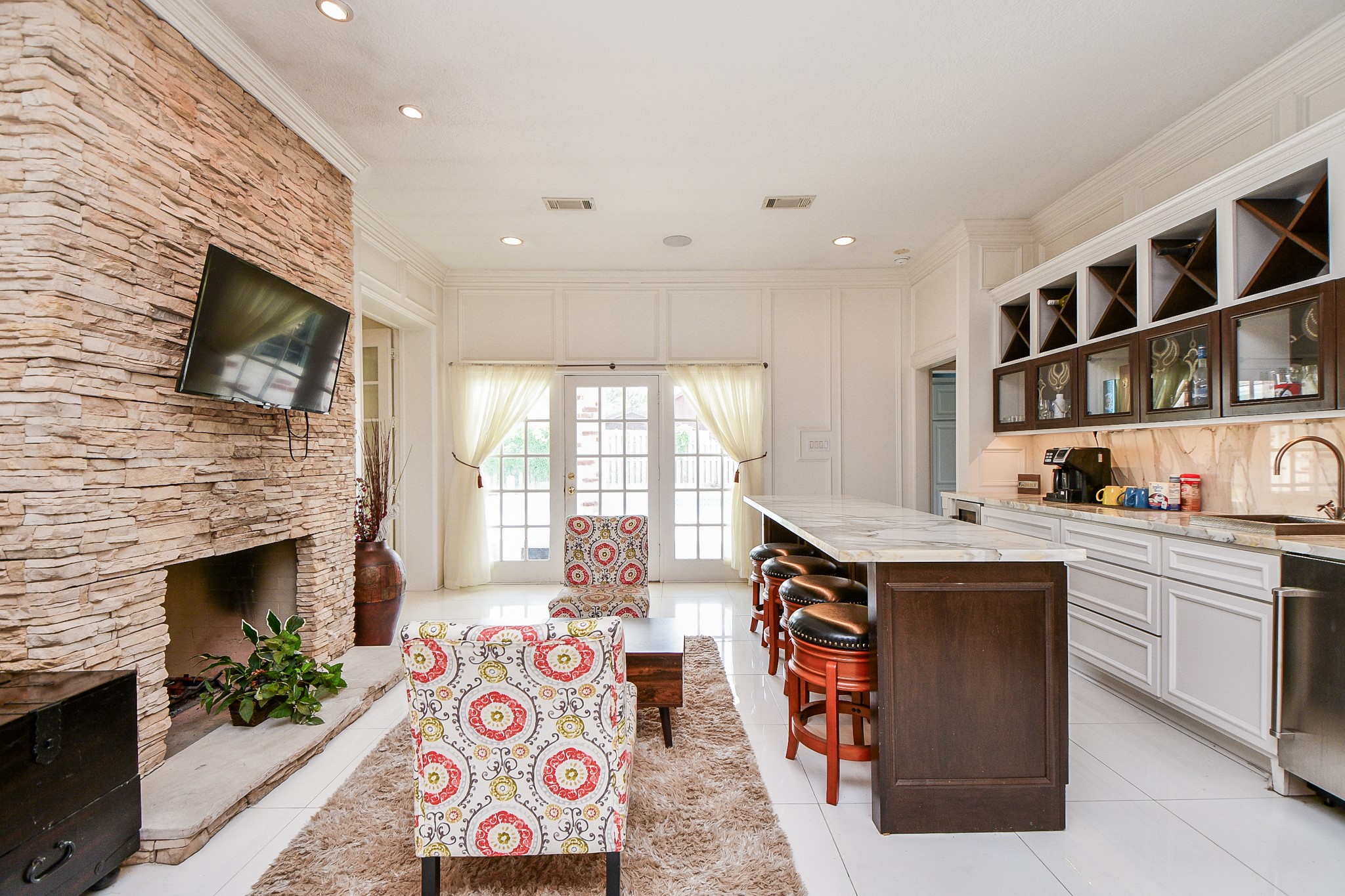 263 Wood Loop Street Houston, TX 77015 - Photo 33 of 45 This inviting living space features a cozy stone fireplace with a mounted TV, an open kitchen with sleek cabinetry and a long island with bar seating. Large windows and French doors provide ample natural light, complemented by stylish furniture and decor.