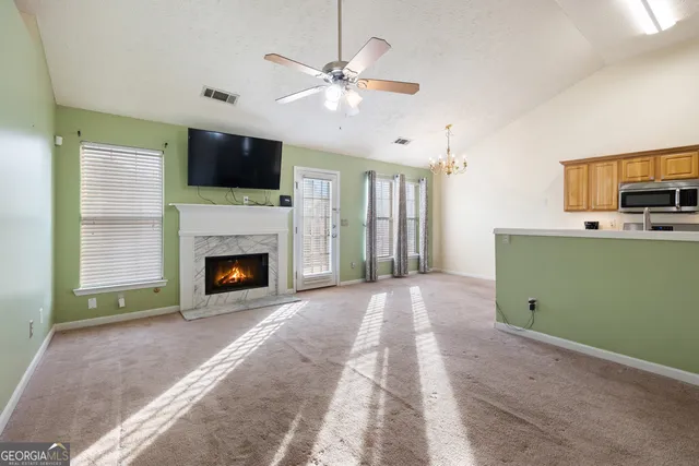 a view of a livingroom with a fireplace a ceiling fan and a kitchen view