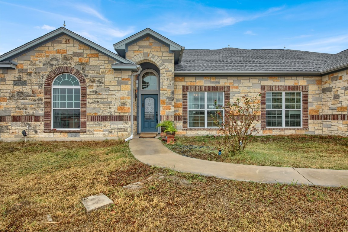 French provincial home featuring a front yard, stone siding, and a shingled roof