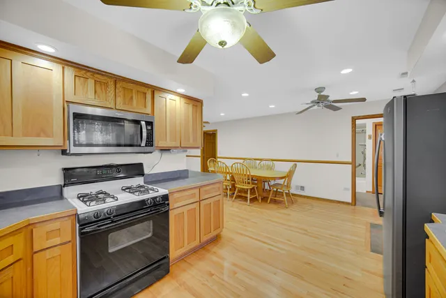 a kitchen with stainless steel appliances granite countertop a stove top oven a sink dishwasher a dining table and chairs with wooden floor