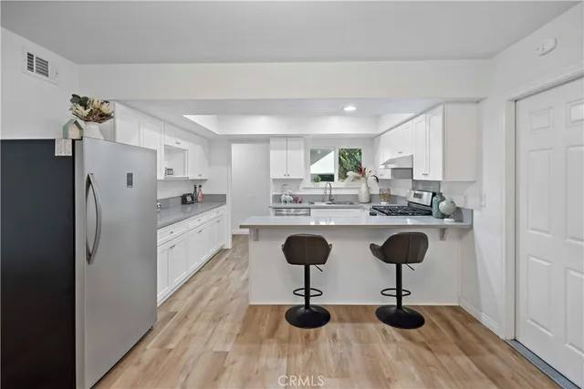 a kitchen with stainless steel appliances kitchen island granite countertop a refrigerator a stove a sink and white cabinets with wooden floor
