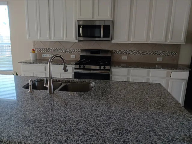 a kitchen with granite countertop a stove a sink and a white cabinets