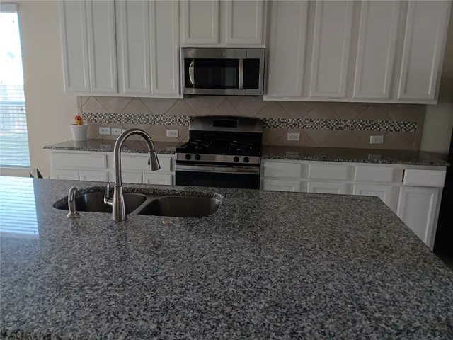 a kitchen with granite countertop a stove a sink and a white cabinets