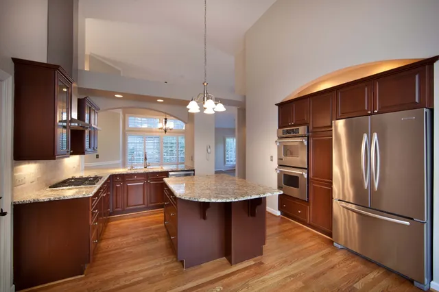 a kitchen with stainless steel appliances granite countertop a refrigerator a sink dishwasher a stove and a dining table with wooden floor