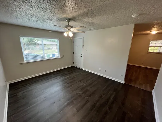 an empty room with wooden floor chandelier fan and windows