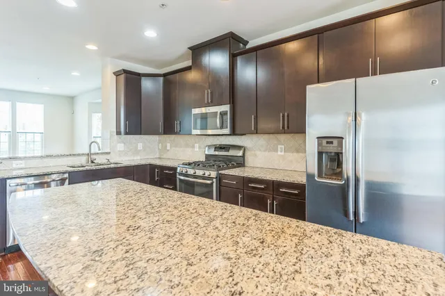 a large kitchen with stainless steel appliances kitchen island granite countertop a refrigerator and a sink