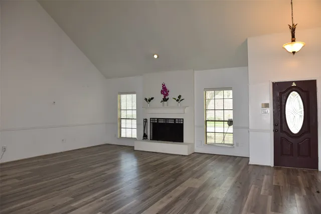 a view of an empty room with wooden floor fireplace and a window