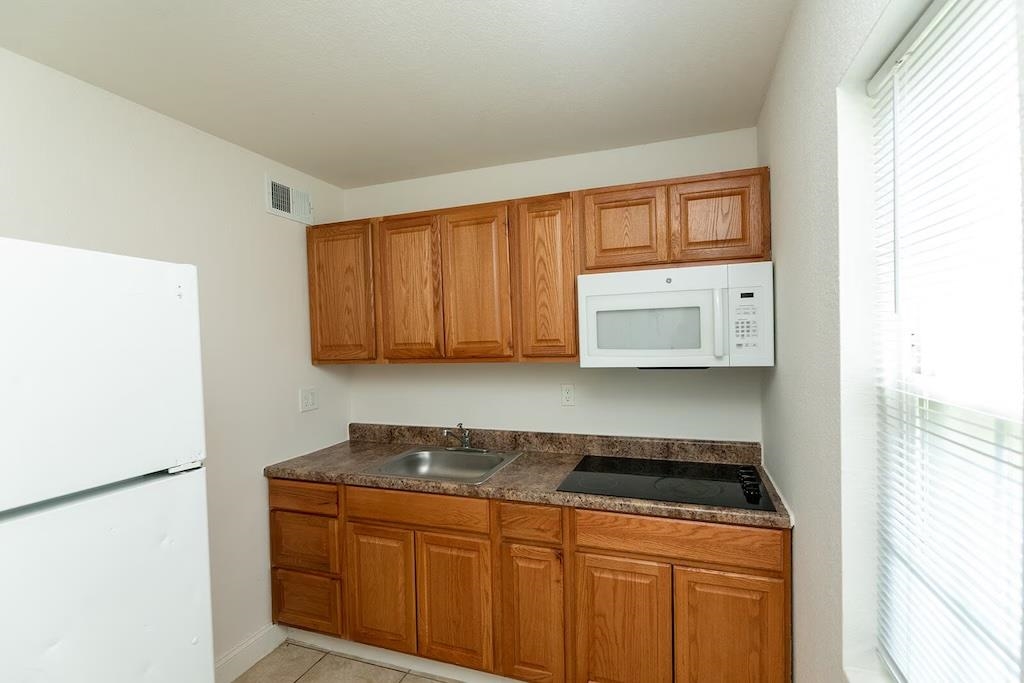 3236 Millington Road Memphis, TN 38127 - Photo 7 of 31 Compact kitchen featuring wood-finish cabinetry, a built-in microwave, an integrated cooktop, a stainless steel sink, and a refrigerator